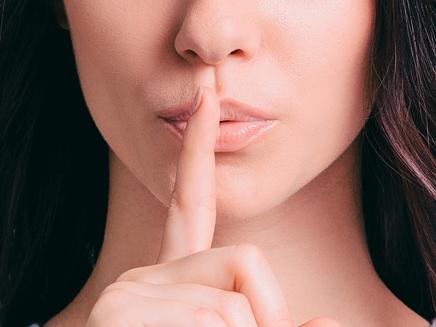 Attractive young woman holding finger on lips while standing against grey background, shh, generic