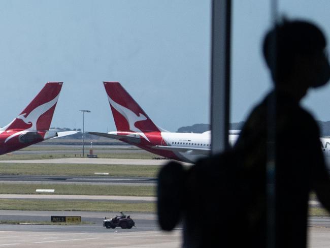 SYDNEY, AUSTRALIA - NewsWire Photos December 9, 2020: Qantas aircraft seen on the runway as a passenger passes through the terminal in the foreground at Sydney International Airport. Picture: NCA NewsWire / James Gourley