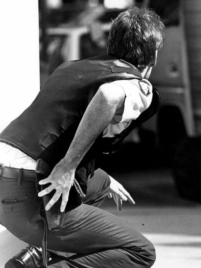 A police office reaches for his gun as he finds cover during the Queen Street massacre. Picture: Bill McAuley