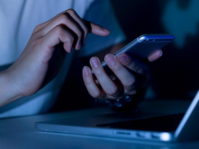 close up young man hand holding smartphone for access by unlock on screen and using laptop for register website on internet in the late night , internet addiction concept