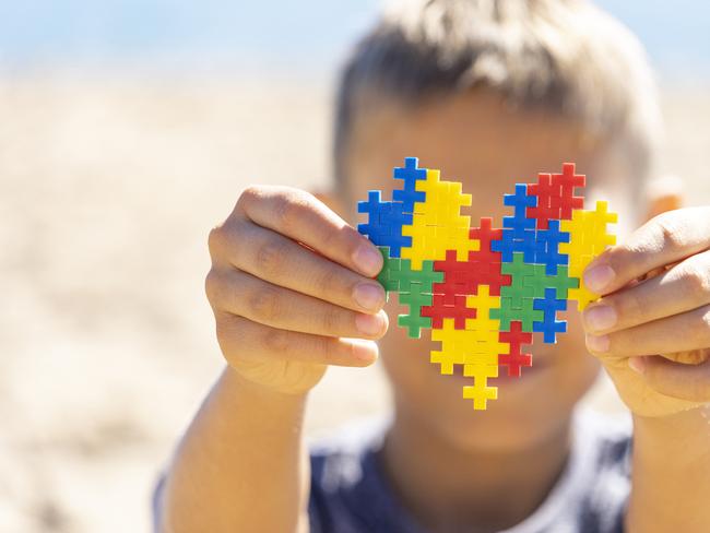 Boy hands holding colorful puzzle heart in front of his face. World autism awareness day concept.