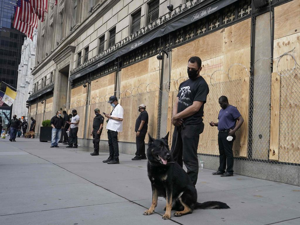 Private security guards with specially trained dogs stand in front of a boarded up and razor wired Saks Fifth Ave. Picture: Timothy A. Clary/AFP