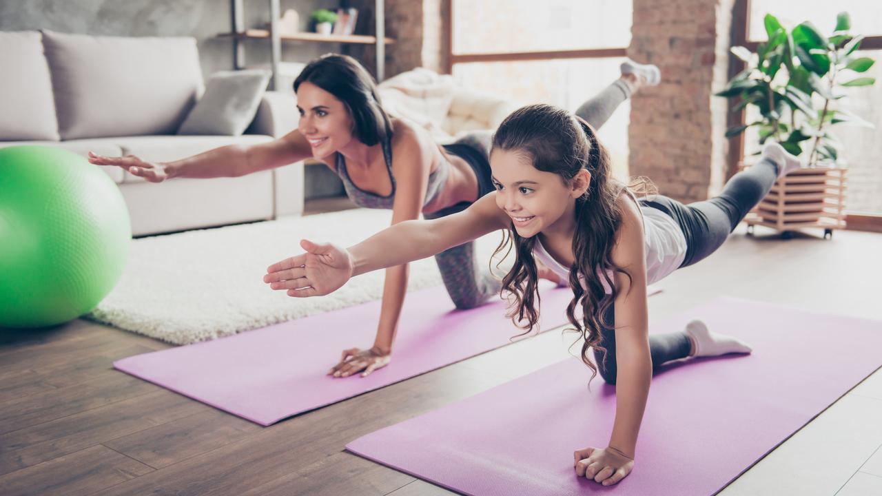Vitality concept. Watch repeat the moves, poses from the helpful video! Cute sweet cheerful joyful with long hair schoolgirl and slim sportive mom are doing stretching exercises in room om purple mats