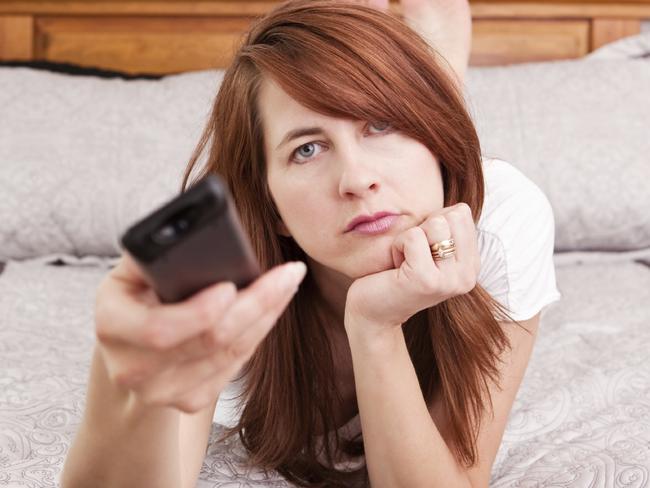 A bored woman flipping through channels as she lays in bed.  Picture: Supplied