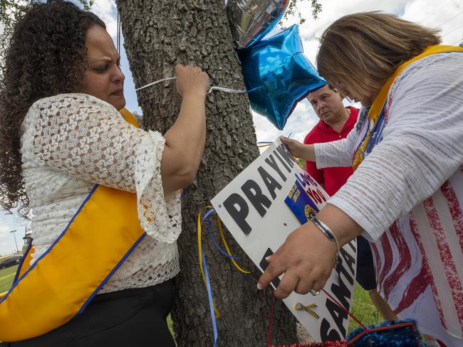 Tanya Diaz, Brock Sanchez and Lucy Martines of League City place flowers, a sign and balloons on a tree outside of Santa Fe High School. Picture: AP