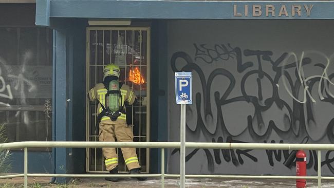 A NSW Fire and Rescue firefighter peers through a locked security gate at the blaze inside the abandoned Belrose Public Library. Picture; Brian Roberts