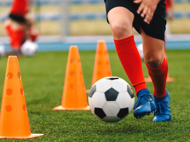 Footballer dribbling ball on training between orange cones. Young football player in sports blue cleats and red socks