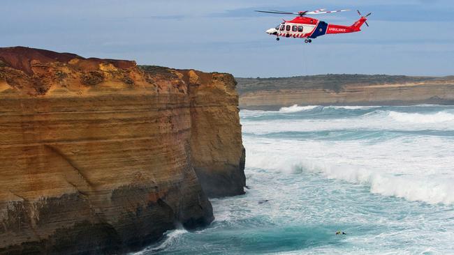 A rescue helicopter winches two men out of the surf at Port Campbell. Picture: Ian McCauley