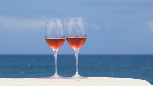 two glasses of rose wine on a whitewashed wall, blue ocean in the background