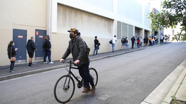 A man coasts his bike past people waiting in line at the Glebe vaccination hub in Sydney. Picture: NCA NewsWire / Dylan Coker