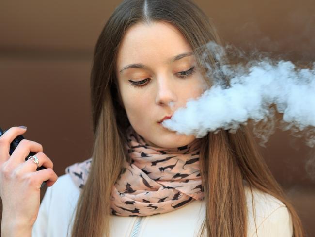 Vape teenager. Young pretty white girl in casual clothing smoking an electronic cigarette opposite modern brown background on the street in the spring. Bad habit. Vaping activity. Close up. i STOCK IMAGE