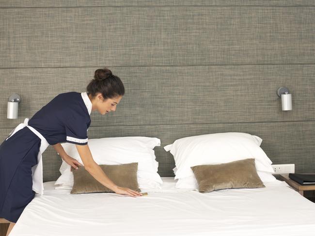 Generic image of a housekeeper making a bed in a room of a hotel.