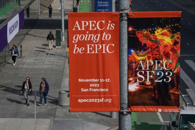 People walk under signs for the Asia-Pacific Economic Cooperation (APEC) meetings ahead of the summit at the Moscone Center in San Francisco