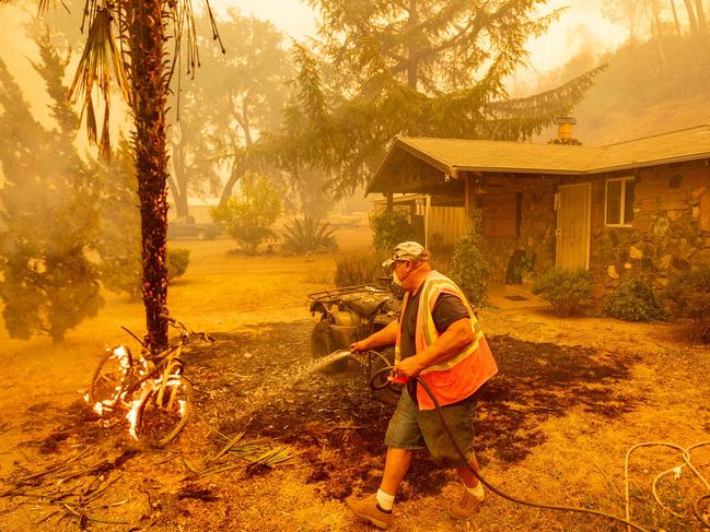 A resident hoses down a burning bicycle and tree as flames in Napa, California as dozens of fires burn out of control throughout Northern California as fire resources are spread thin. Picture: AFP