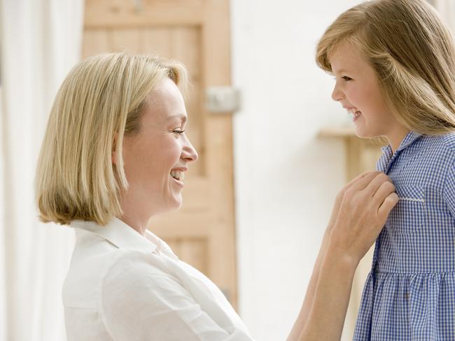 Mum getting child ready for school. Woman in front hallway fixing young girl's dress kneeling down looking at each other smiling.