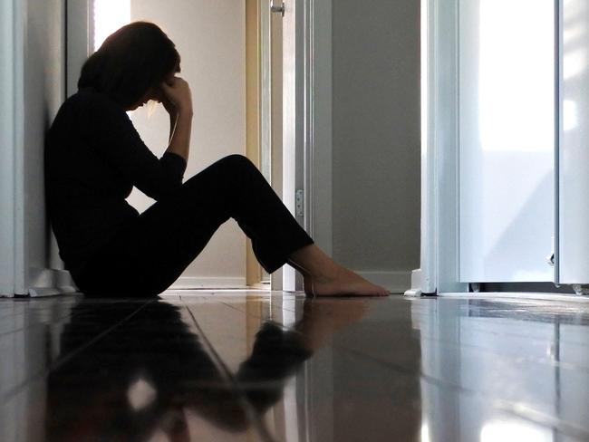 Sad adult woman sitting on dark home corridor floor.