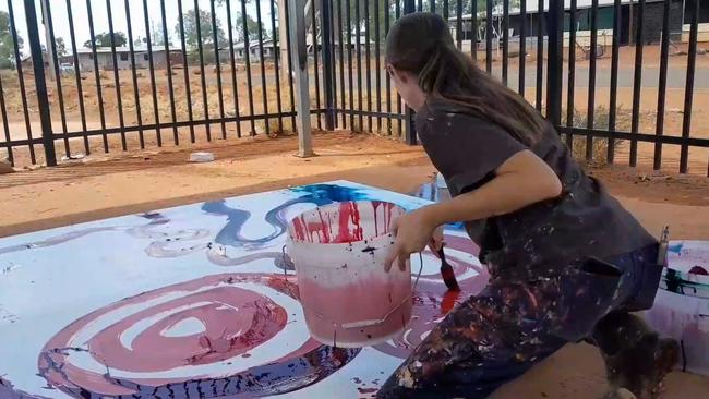 A still taken from a video where the non-Indigenous Rosie Palmer, manager of Tjala Art, contributes to a painting by Indigenous artist Yaritji Young.