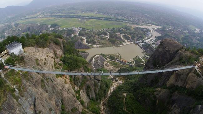 PINGJIANG, CHINA - SEPTEMBER 24: (CHINA OUT) Tourists walk on a suspension bridge made of glass at the Shiniuzhai National Geological Park on September 24, 2015 in Pingjiang County, China. The 300-meter-long glass suspension bridge, with a maximum height of 180 meters, opened to the public on Thursday. (Photo by ChinaFotoPress/ChinaFotoPress via Getty Images)