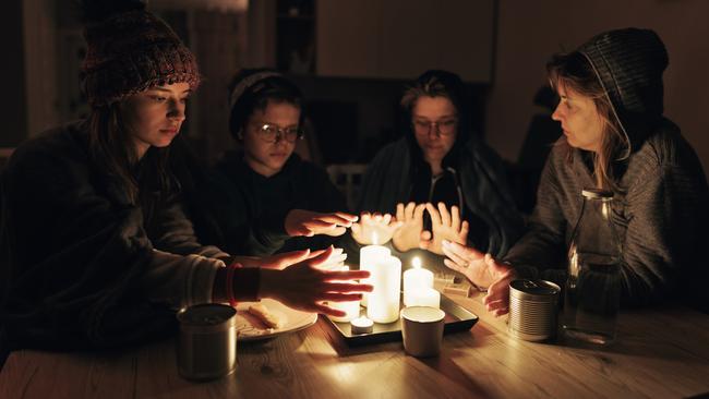 During the energy crisis family is sitting by the table, lit by candles. Everyone is wearing warm clothes because of heating problems during the power outage. They are eating dry biscuits and warming hands from the candle flame. Canon R5 istock image ,