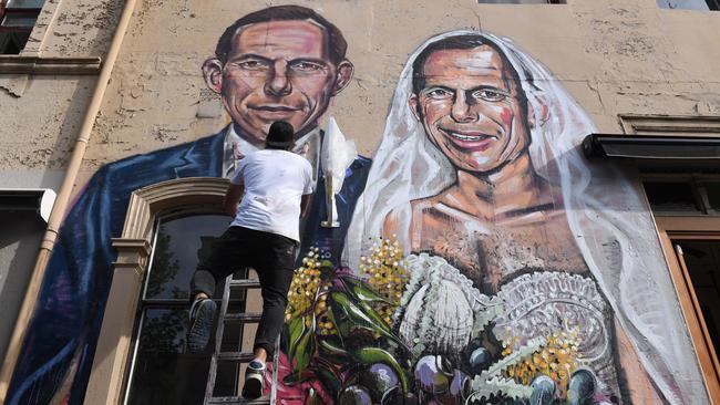 Artist Scott Marsh finishing off his mural of former prime minister Tony Abbott getting married to himself in Redfern.