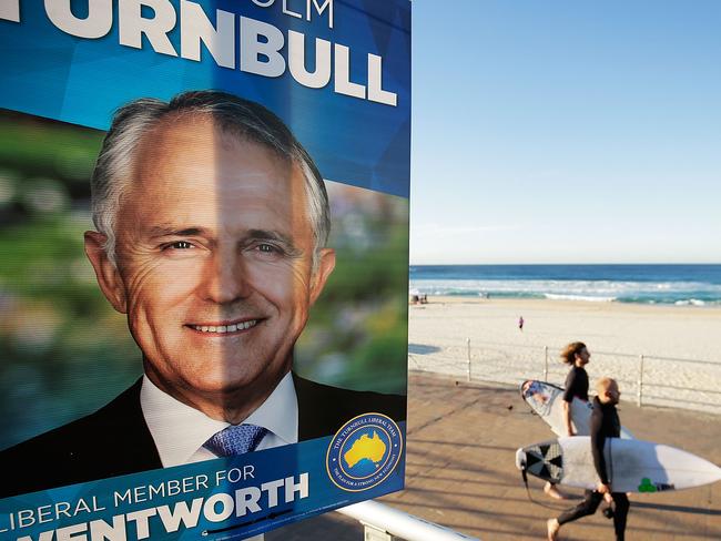 Surfers walk past an election poster at Bondi Beach in the electorate of Wentworth as voters head to the polls today. Picture: Mark Metcalfe/Getty Images)