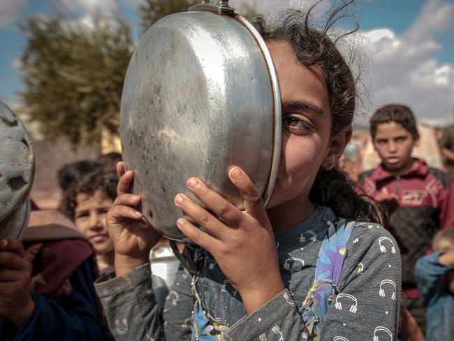 IDLIB, SYRIA - OCTOBER 07 : A Syrian girl covers her face with a cooking pot as they queue to receive food aid in Idlib, Syria on October 07, 2019. While more than 820 million people worldwide struggle with hunger, over 670 million adults and 120 million children aged 5 to 19 years have obesity. Food insecurity raises concerns about "acute hunger" caused by high levels of malnutrition and "unhealthy nutrition", which increases the risks of illness and death. According to Food and Agriculture Organization of the United Nations; more than 820 million people, or one in 9, are struggling with hunger worldwide, with an increasing number of malnourished people. As thousands of people have lost their lives in the clashes in Syria, the humanitarian crisis increases day by day. Syrians, who sheltered in safe zones due to the civil war, have hard time reaching food. (Photo by Muhammed Said/Anadolu Agency via Getty Images)