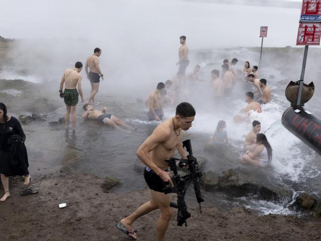 An Israeli soldier carries some weapons as they and residents enjoy a hot spring in the Golan Heights following a ceasefire agreement. Picture: Getty Images