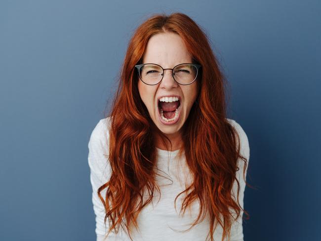 Angry young woman throwing a temper tantrum yelling at the camera with a furious expression over a blue studio background with copy space