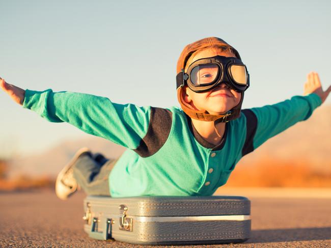 A young boy dressed in retro clothing and flying goggles dreams of flying on an exotic vacation at a far off destination. He is outstretching his arms like an airplane while on top of a suitcase and he has a happy expression on his face. Image taken in Utah, USA. Picture: iStock. Picture: iStock.