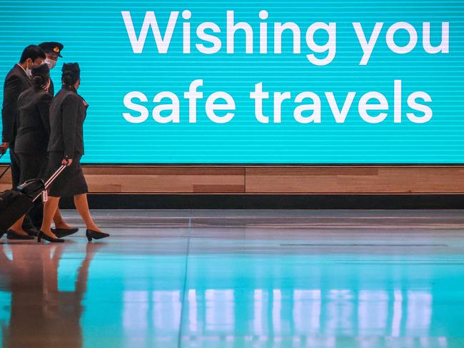 This picture taken on September 29, 2020 shows Qatar Airlines flight crew members wearing face masks as a preventive measure against the COVID-19 novel coronavirus as they walk past an illuminated sign in the Sydney International Airport in Sydney. (Photo by David GRAY / AFP)