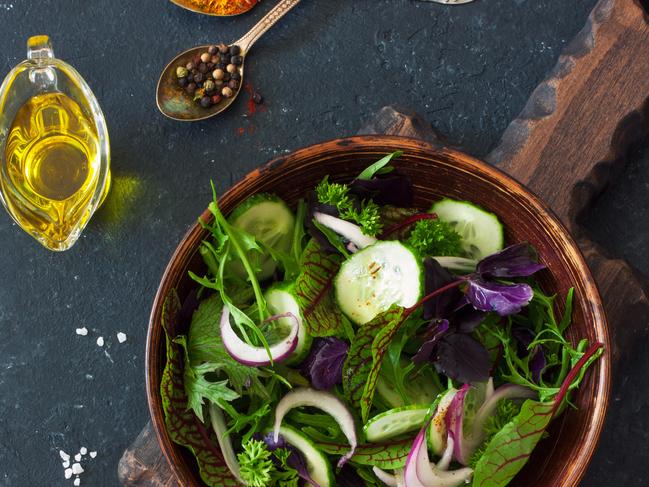 Fresh lettuce, arugula, frisee, basil, cucumber and onions salad in a clay bowl over black stone background.Vegan food. Top view.