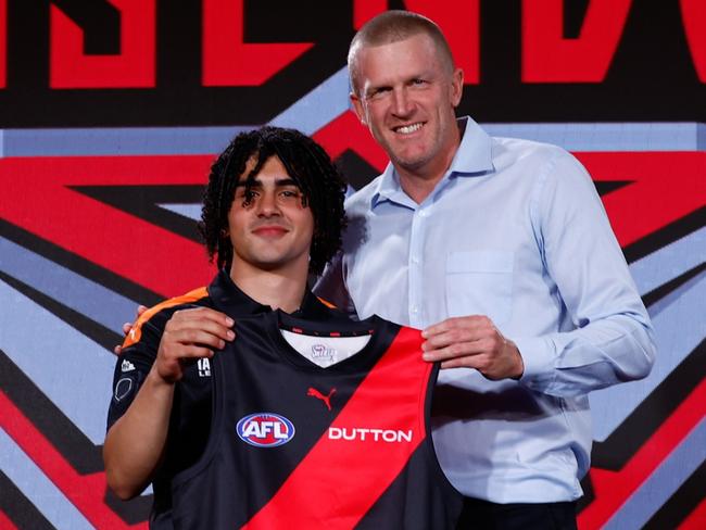 MELBOURNE, AUSTRALIA - NOVEMBER 20:  The number 13 pick, Isaac Kako is presented his Essendon  jumper by Dustin Fletcher during the 2024 Telstra AFL Draft at Marvel Stadium on November 20, 2024 in Melbourne, Australia. (Photo by Michael Willson/AFL Photos via Getty Images)