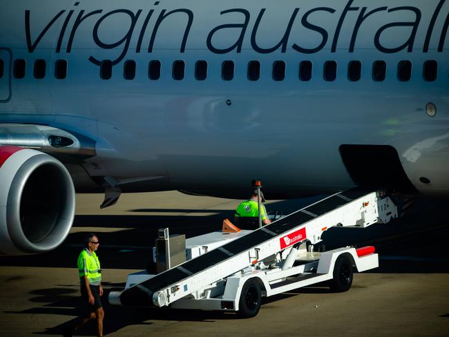 Baggage handlers prepare to unload freight from a Virgin Australia aircraft on the tarmac at Brisbane International airport on April 21, 2020. - Cash-strapped Virgin Australia collapsed on April 21, making it the largest carrier yet to buckle under the strain of the coronavirus pandemic, which has ravaged the global airline industry. (Photo by Patrick HAMILTON / AFP)