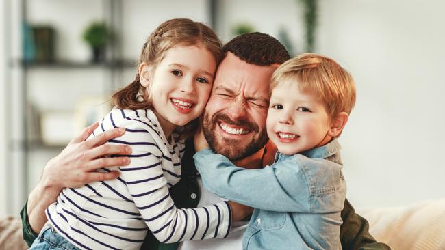 Adorable smiling little sister and brother hugging happy dad with gift box in hand while giving congratulations on fathers day at home