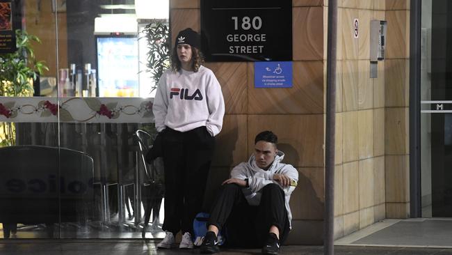 The victim’s friends sit stunned outside the foyer of the building. Picture: Gordon McComiskie