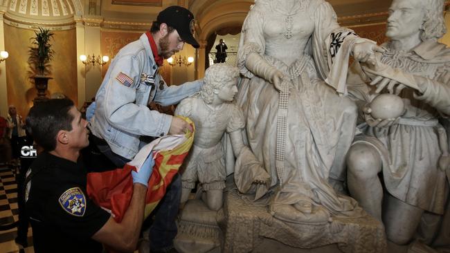 A demonstrator is removed from the statue of Queen Isabella and Christopher Columbus in the rotunda of the Capitol, by a California Highway Patrol officer. Picture: AP