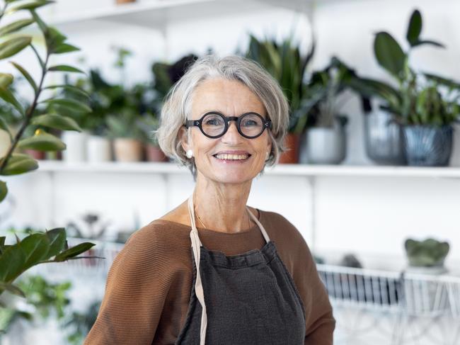 Portrait of senior female florist at small business flower shop. Happy mature woman wearing apron working in a small flower store; working in retirement happy retiree worker generic