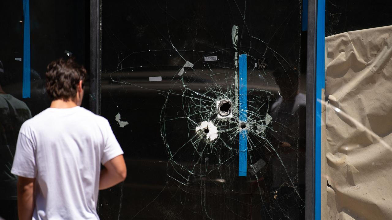 A pedestrian walks past bullet holes in the window of a store front on South Street in Philadelphia, Pennsylvania the day after a mass shooting. Picture: Kriston Jae Bethel / AFP