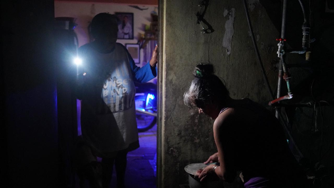 A woman boils water while another lights her with a mobile phone in Matanzas, Cuba. Picture: Antonio Levi/AFP