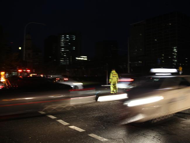 A lone police officer directing Adelaide CBD traffic in darkness. Picture: Emma Brasier