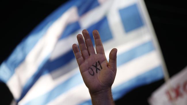 FILE - In this July 3, 2015 file photo, a demonstrator raises his hand with the word ''No'' written on it as a Greek flag waves behind during a rally organized by supporters of the No vote in Athens. From Grexit to Grimbo, Greece’s debt crisis has spawned its own awkward argot. (AP Photo/Petros Giannakouris, File)