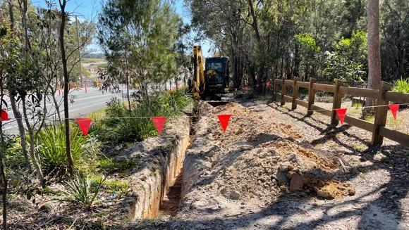 An excavator digs a trench on the fence line of the cemetery.