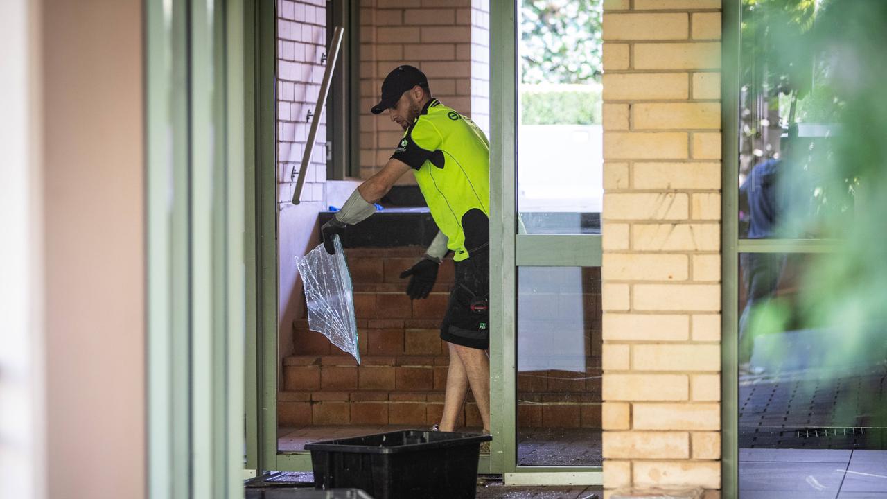 A worker cleans up broken glass from a smashed window at the entrance to the apartment block. Picture: Julian Andrews