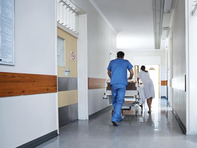 Rearview shot of hospital staff wheeling a patient in a gurney down a corridor