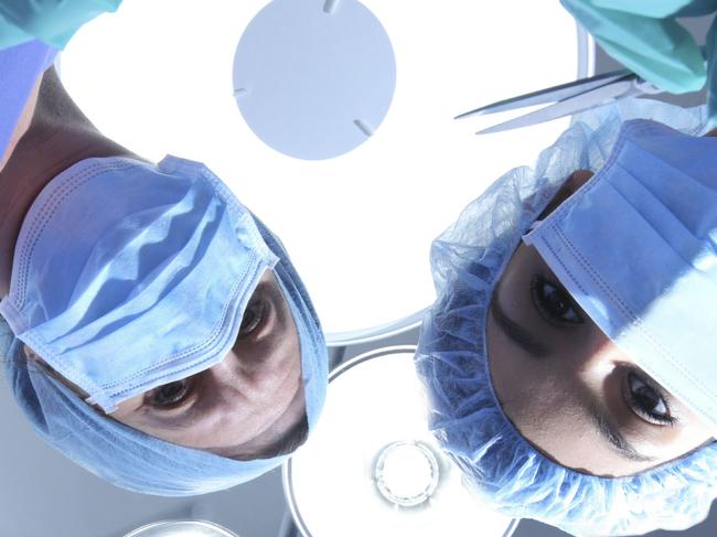 Generic of team of medical staff, doctors, nurses, surgeons, etc, looking down on a patient about to undergo surgery (operation) in a hospital operating theatre as the overhead lights blaze away. Picture: Thinkstock