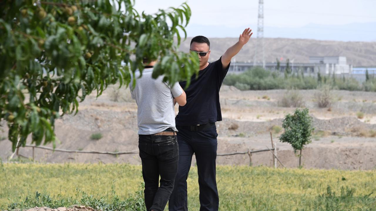 An AFP video journalist being escorted away from filming buildings at the Artux City Vocational Skills Education Training camp, seen in the distance. Picture: AFP