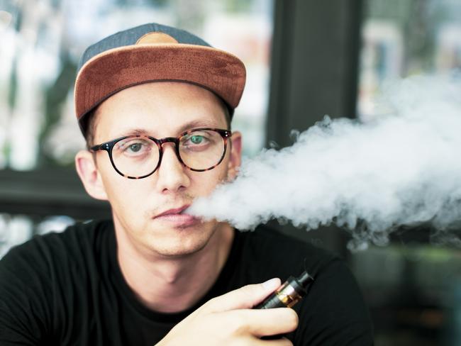 Young European man looking at the camera and smoking vapor