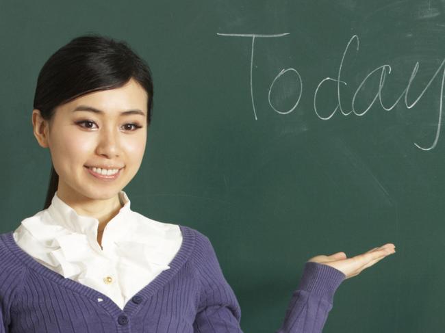 Teacher Standing By Blackboard In Chinese School Classroom