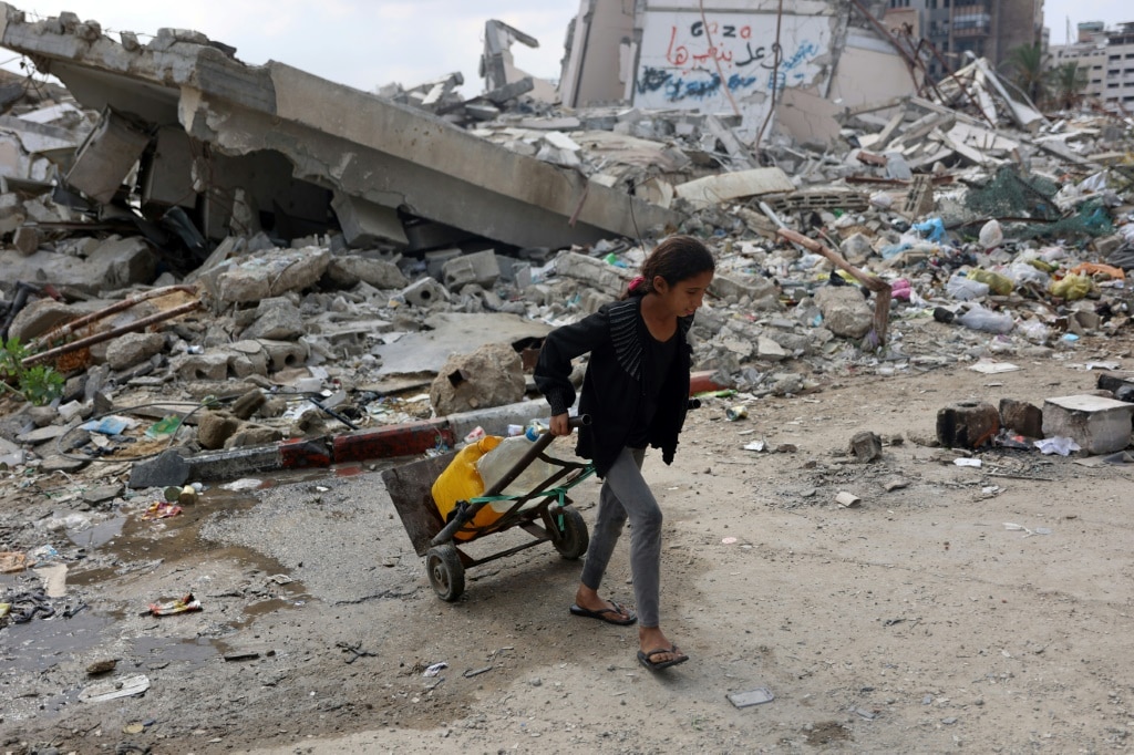 A Palestinian girl transports clean water past a destroyed building in Gaza City, in the territory's north