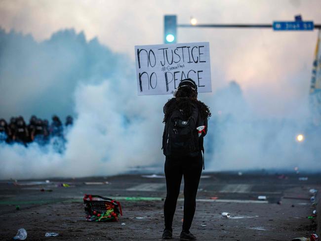 Smoke rises near a demonstrator holding a sign and facing a row of police near the 5th police precinct during a demonstration to call for justice for George Floyd, in Minneapolis, Minnesota. Picture: AFP